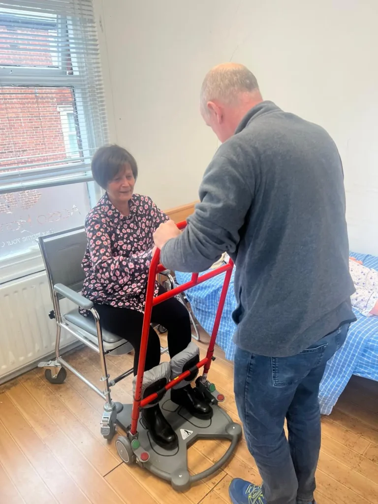 A carer supporting a client to stand using a mobility frame in her bedroom